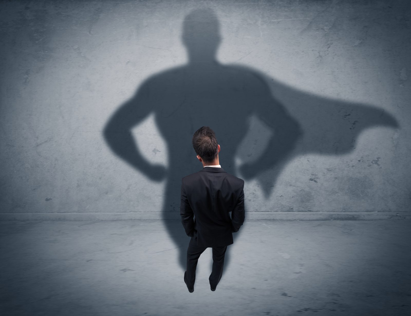 A man in a suit casts the shadow of a caped figure on a concrete wall